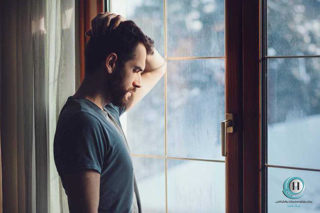 مردی که اضطراب پنهان دارد و با ناراحتی از پنجره به بیرون نگاه میکند