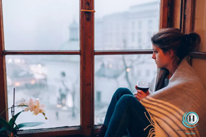 زنی که درگیر غم زمستانی است و از پنجره به بیرون نگاه میکند.